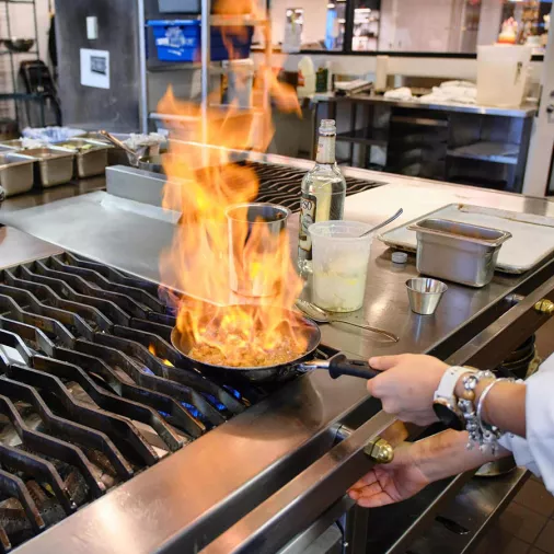 A chef cooks with a pan on fire